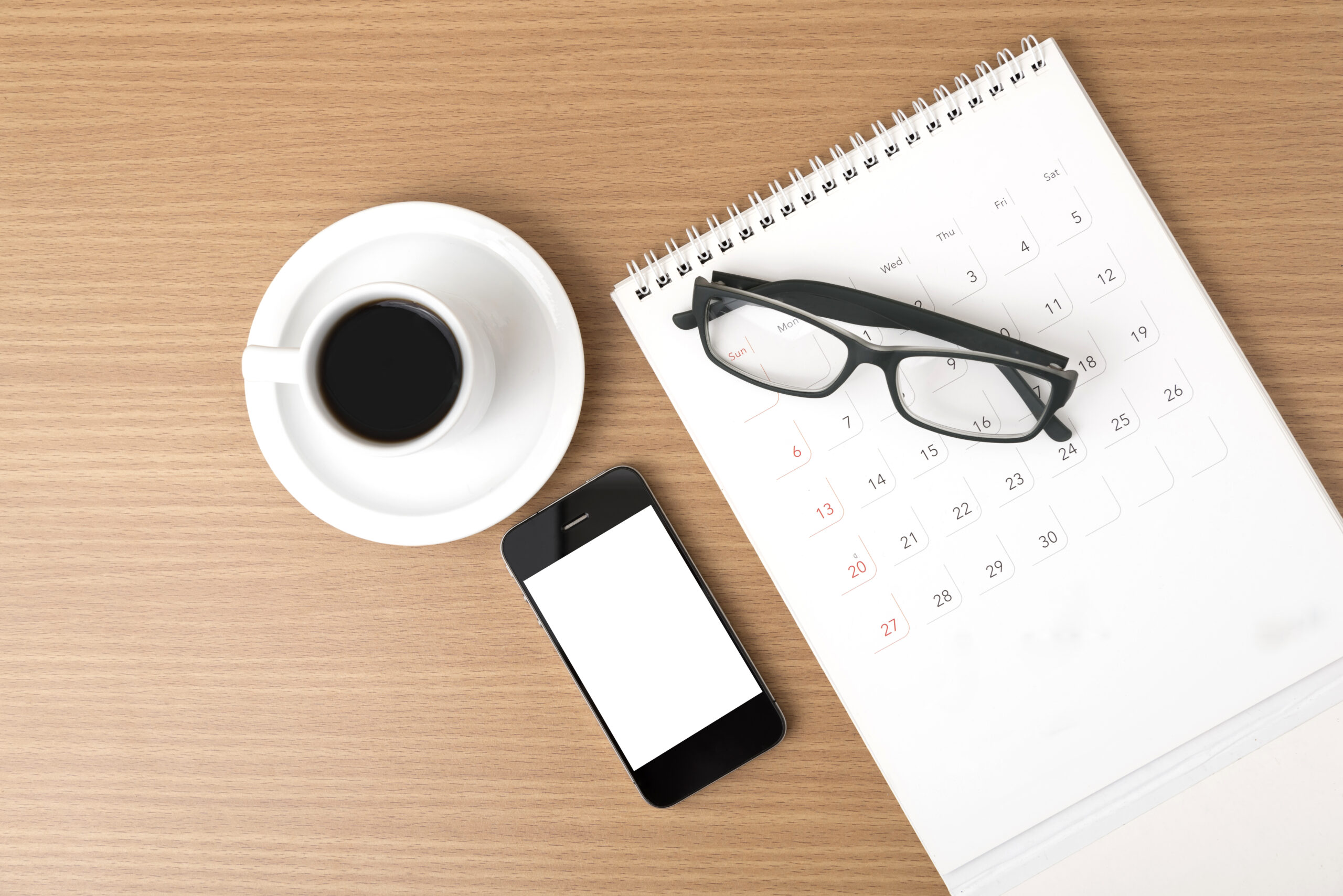 Calendar, smartphone, glasses, and coffee on desk, symbolizing creating an effective pediatric board exam study schedule for success.